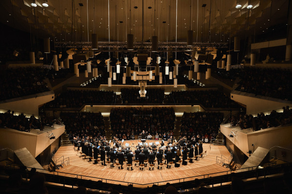 Fernaufnahme in einem großen Konzertsaal, der Berliner Philharmonie.  Chor und Orchester und Publikum im Hintergrund.